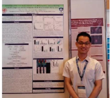 Man with conference badge smiling beside large research posters